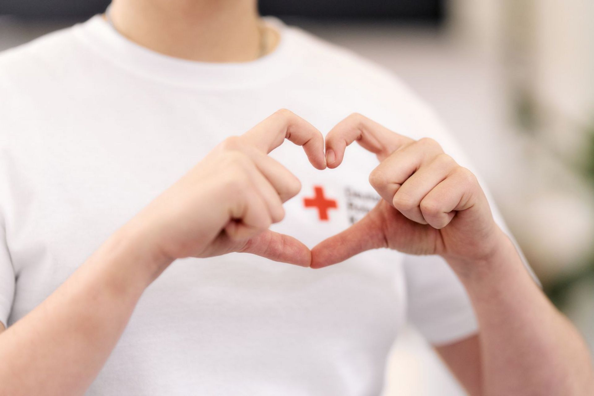 Zwei Hände formen ein Herz, welches über dem DRK Logo auf dem T-Shirt gehalten wird