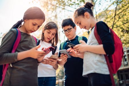 Jugendliche_Smartphones_social_media Vier Jugendliche stehen zusammen und beugen sich über ihre Smartphones.